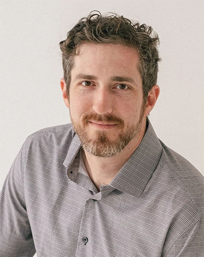 A headshot image of Dr. Will Flannary, looking into the camera and wearing a long sleeve grey shirt.