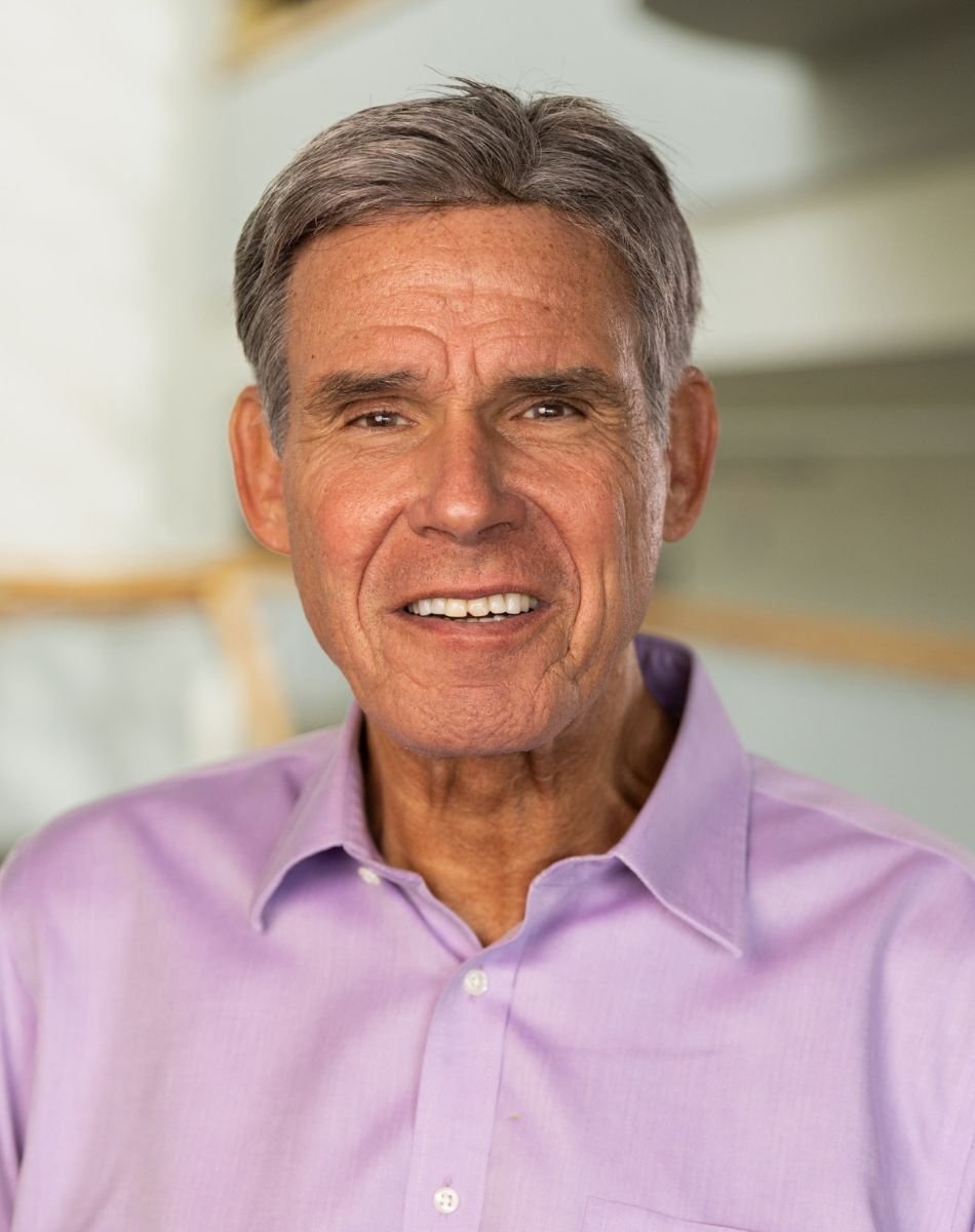 A headshot image of Eric Topol, wearing a lavender collared shirt against a blurred interior background.