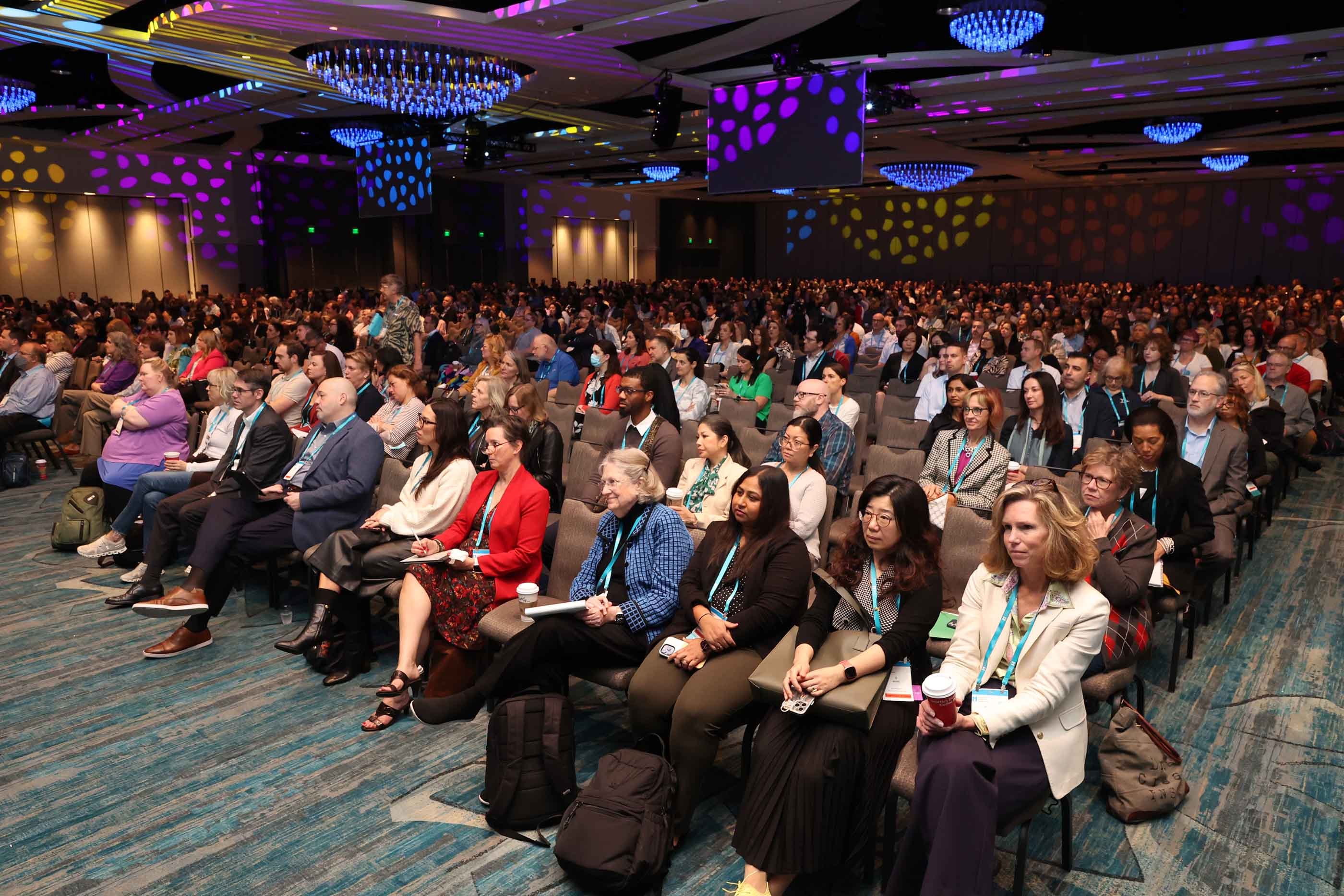 Crowd of attendees sitting and watching a keynote address in a conference ballroom.