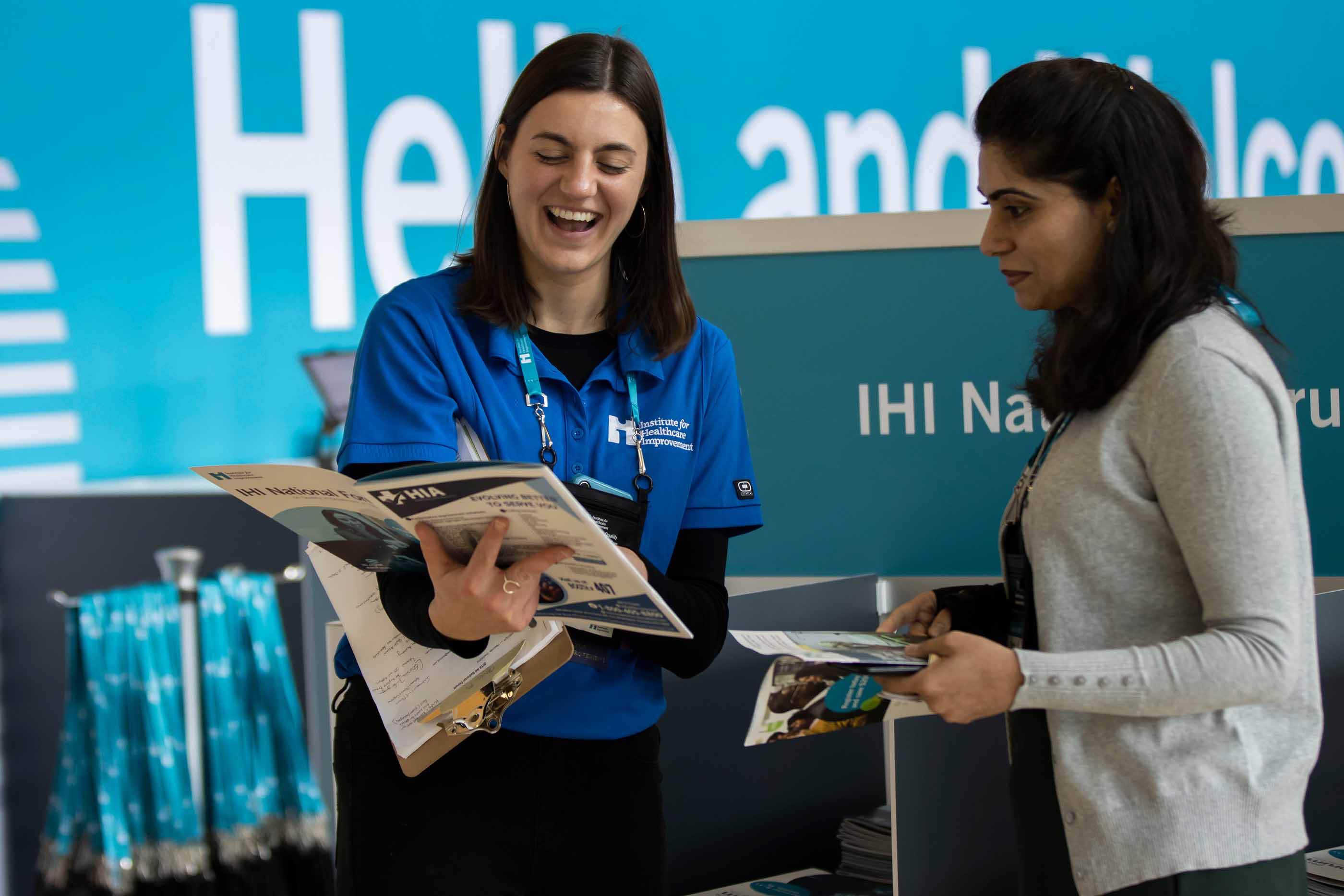 A female IHI staff member in a blue shirt assisting a conference attendee using that year's program booklet.