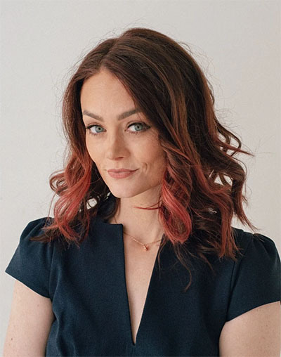 A headshot image of Kristin Flannary, looking into the camera and wearing a black shirt and gold necklace.
