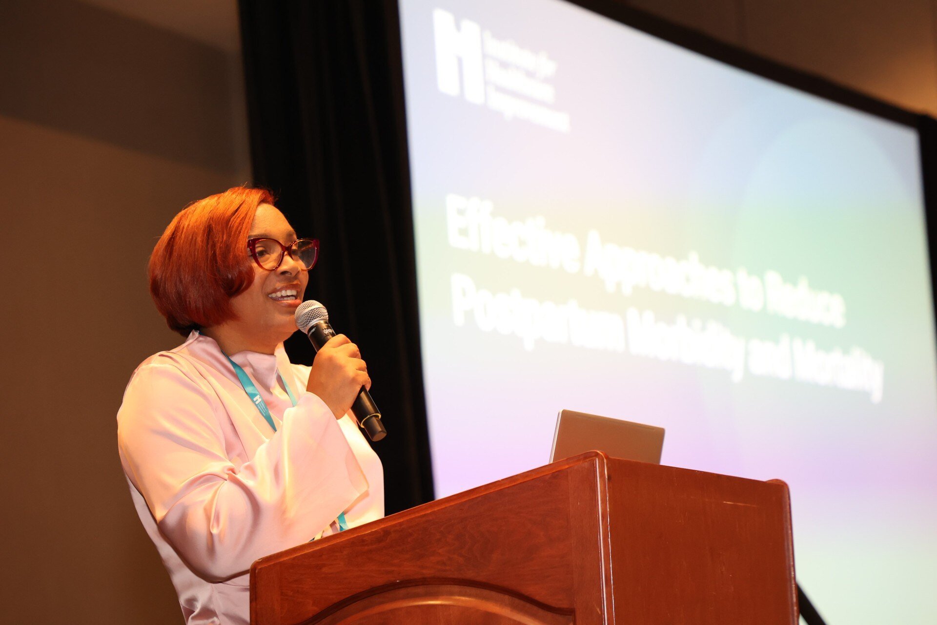 A female presenter behind a podium hosting a session on postpartum health.